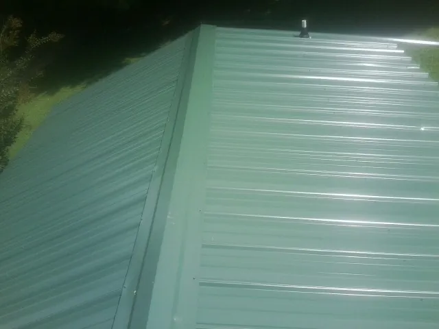 New green metal panels meeting at the ridge of a roof — Flat Roof Repair work by our crew in West Liberty